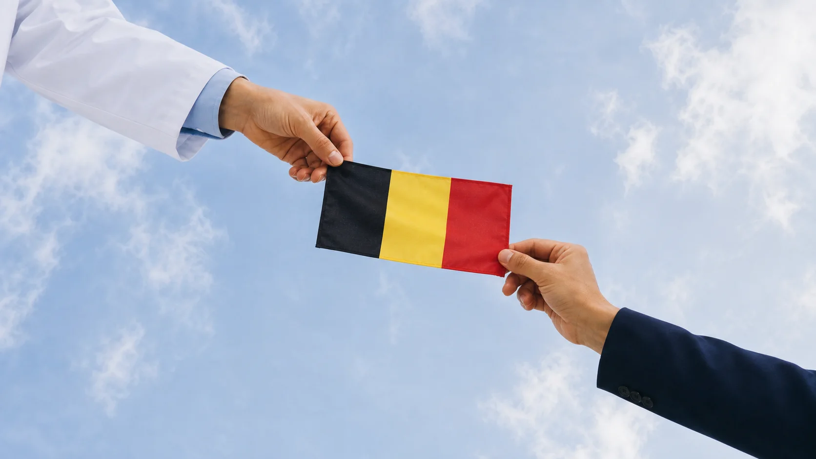 Une médecin et un agent communal tiennent ensemble le drapeau belge sous un ciel clair.